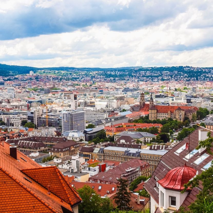 Erhöhter Panoramablick auf eine dichte europäische Stadt mit roten Ziegeldächern, Kirchtürmen und Hügeln im Hintergrund